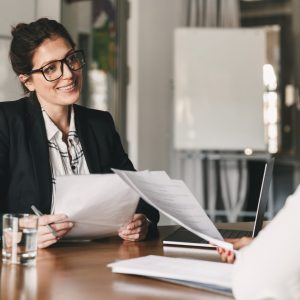 Portrait of smiling businesswoman holding resume and talking to female candidate during corporate meeting or job interview - business, career and placement concept